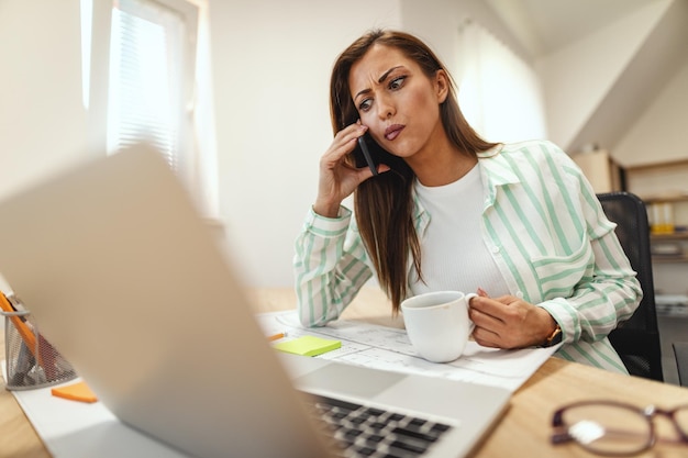 Un'imprenditrice pensierosa sta parlando su uno smartphone in ufficio ed è preoccupata per qualcosa che ha sentito.