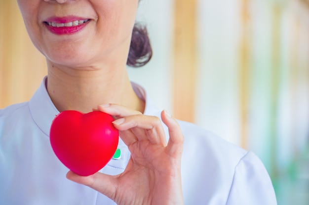Un&#39;infermiera che tiene il giocattolo rosso del cuore. La foto mostra il principio di preoccuparsi e di buona salute.