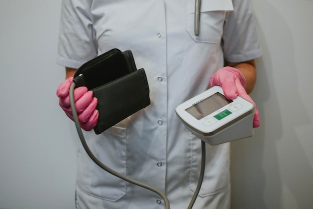 Un'infermiera con un cappotto bianco e guanti rosa tiene in mano un dispositivo per misurare la pressione sanguigna dei pazienti