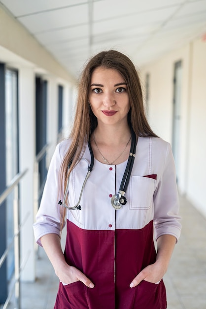 Un'infermiera dall'aspetto attraente in uniforme sta aspettando i pazienti nella clinica in corridoio