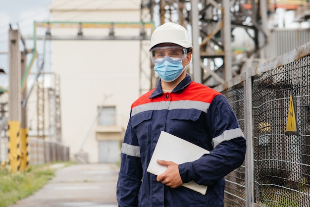 Un ingegnere della sottostazione elettrica ispeziona le moderne apparecchiature ad alta tensione in una maschera al momento della pissemia. Energia. Industria.