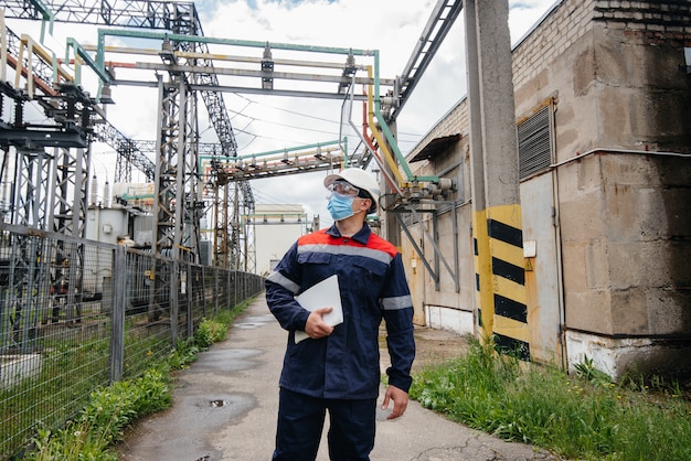 Un ingegnere di sottostazione elettrica ispeziona le moderne apparecchiature ad alta tensione in una maschera al momento della pondemia. Energia. Industria.