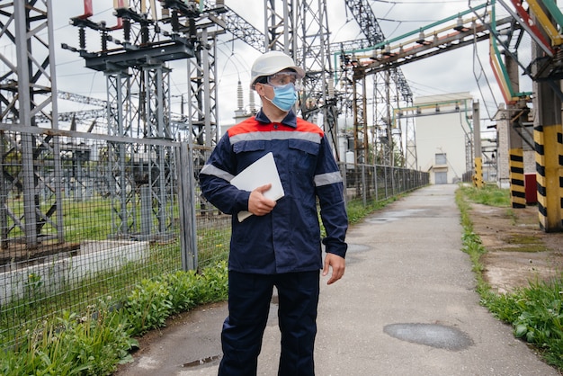 Un ingegnere di sottostazione elettrica ispeziona le moderne apparecchiature ad alta tensione in una maschera al momento della pondemia. Energia. Industria.