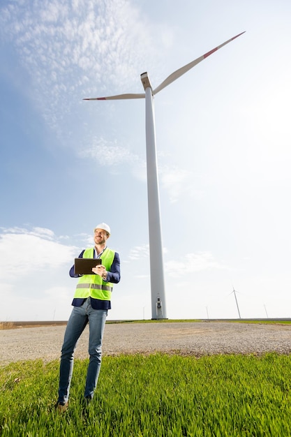 Un ingegnere ispeziona l'efficienza delle turbine eoliche in un vasto campo verde in una giornata di sole