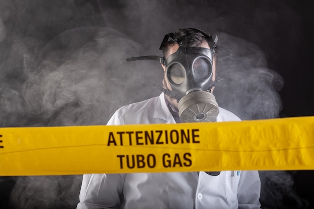 Un ingegnere medico che indossa una maschera antigas esperta nella crisi delle fughe di gas dirige l'emergenza durante il caos. Sul nastro giallo la scritta "attenzione tubo gas"