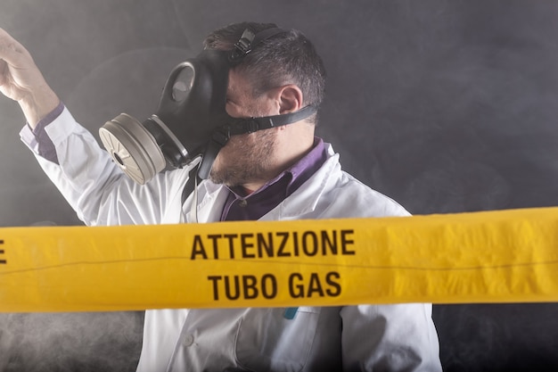 Un ingegnere medico che indossa una maschera antigas esperta nella crisi delle fughe di gas dirige l'emergenza durante il caos. Sul nastro giallo la scritta "attenzione tubo gas"