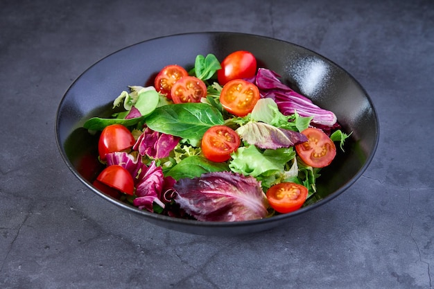 Un'insalata di lattuga pomodoro agnelli lattuga e scarola su un piatto nero su uno sfondo di ardesia