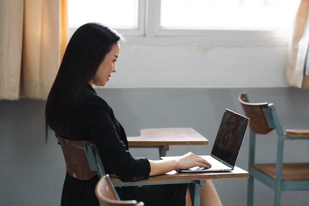 Un'insegnante asiatica di mezza età seduta in classe con un laptop sulla scrivania dell'università