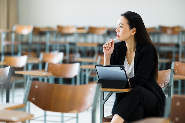 Un'insegnante donna con un tablet siede in un'aula vuota all'università. in attesa di insegnare agli studenti in classe