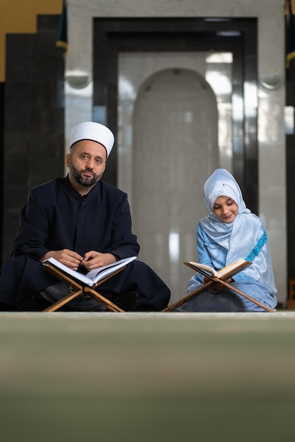 Un insegnante musulmano che insegna a una bambina a leggere un libro sacro del Corano all'interno della moschea