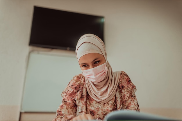 Un insegnante musulmano stanco con una maschera protettiva è seduto in classe Messa a fuoco selettiva Foto di alta qualità