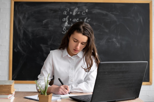 Un'insegnante o una studentessa studia a distanza online in classe seduto alla scrivania con un laptop che prende appunti guardando una lezione o ascoltando un webinar sulla rete Concetto di formazione online