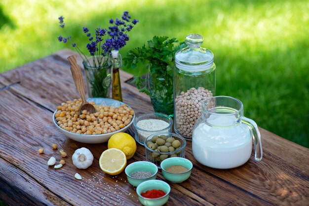 Un insieme di ingredienti per la preparazione di snack hummus: ceci, tahini, spezie, aglio, prezzemolo, olio d'oliva su un tavolo di legno. Ricetta per un antipasto vegetariano mediterraneo.