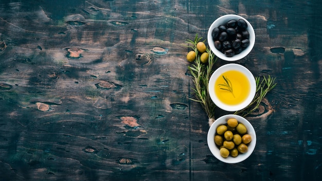 Un insieme di olive e olio d'oliva e rosmarino Olive verdi e olive nere Su uno sfondo di legno nero Spazio libero per il testo