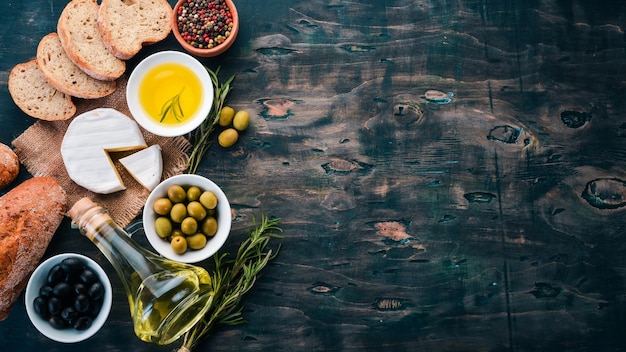 Un insieme di olive olio d'oliva pane formaggio e spezie su uno sfondo di legno nero Spazio libero per il testo