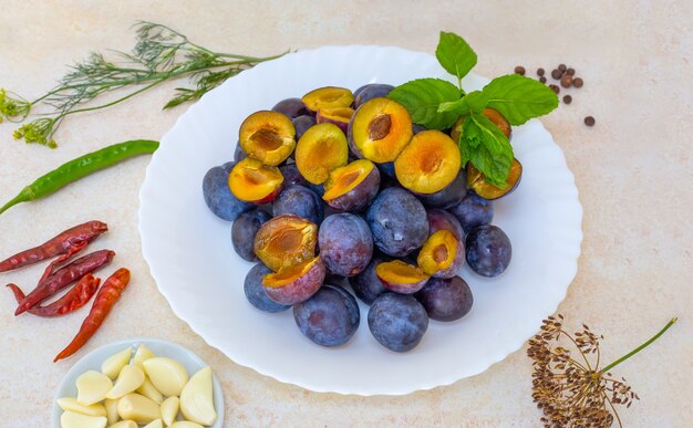 Un insieme di prodotti per la preparazione della salsa georgiana alla frutta piccante tkemale. Prugne in un piatto, aglio e peperoni nelle vicinanze.