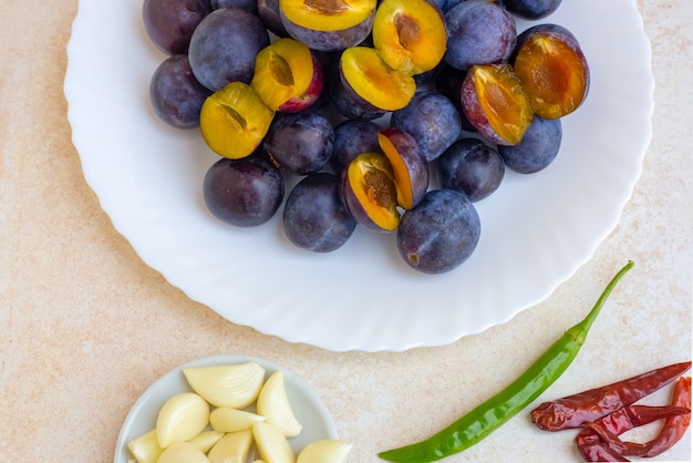 Un insieme di prodotti per la preparazione della salsa georgiana alla frutta piccante tkemale. Prugne in un piatto, aglio e peperoni nelle vicinanze.