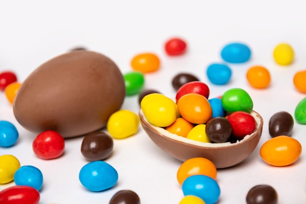 Un intero e mezzo di un uovo di cioccolato incrinato ripieno di caramelle multicolori su uno sfondo bianco con caramelle multicolori