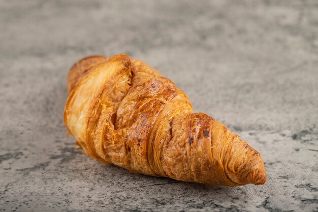 Un intero gustoso croissant burroso posto su un tavolo di pietra.