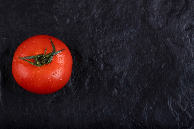 Un intero pomodoro fresco rosso posto su uno sfondo nero.