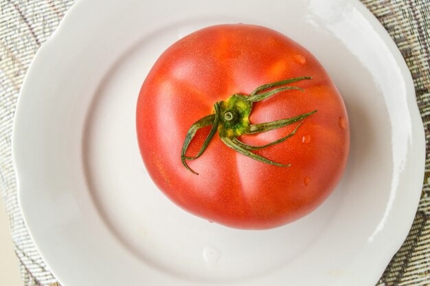Un intero pomodoro rosso fresco su un piatto bianco, vista dall'alto.