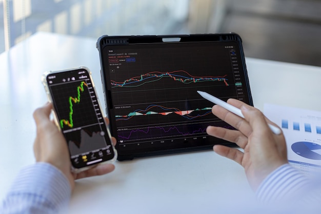 Un investitore sta guardando i grafici delle azioni su telefoni cellulari e tablet, è un investitore in azioni, fa trading di azioni analizzando i grafici e utilizzando gli indicatori per entrare nelle operazioni. Idea di investimento azionario.