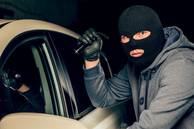 Un ladro vestito con una maschera nera, puntando una torcia verso il conducente in macchina. Il concetto di criminalità.