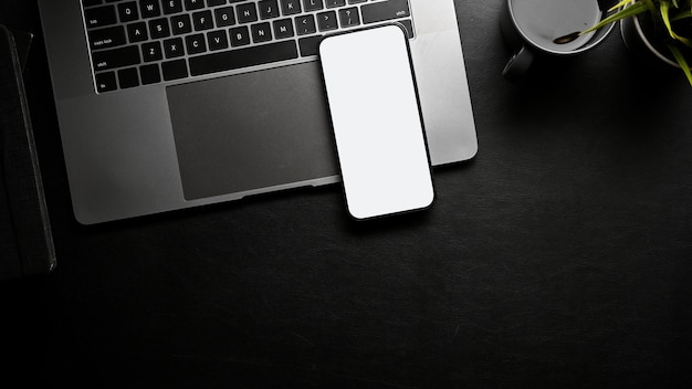 Un laptop mockup con schermo bianco per smartphone e spazio per la copia su un'area di lavoro nera