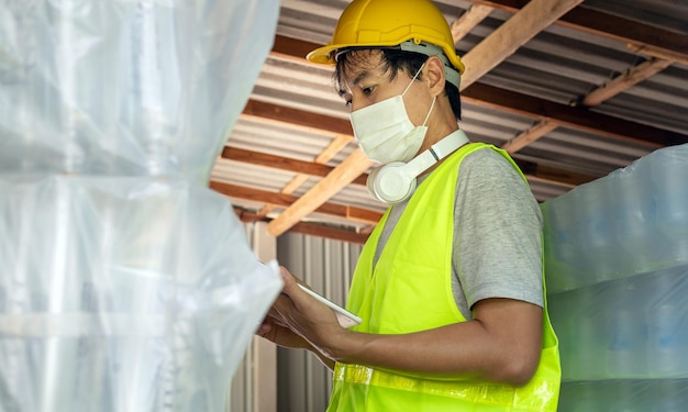 Un lavoratore che controlla lo stock di bottiglie di plastica nel magazzino Utilizzo del tablet per aggiornare lo stock online