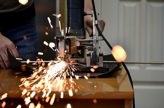 Un lavoratore che taglia un tubo di metallo in due pezzi e molte scintille che volano dritte nel primo piano della telecamera.