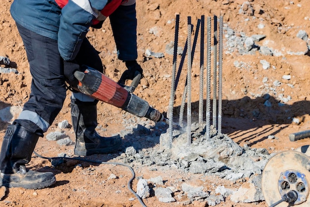 Un lavoratore con un martello pneumatico rompe i pali di cemento Abbattimento della testa del palo con un utensile manuale Preparazione dei pali per il montaggio della fondazione