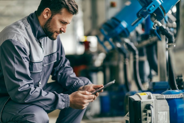 Un lavoratore del settore è accovacciato accanto a una macchina e la regola su un tablet