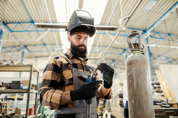 Un lavoratore dell'industria pesante che regola il saldatore e si prepara a saldare le parti metalliche nella struttura