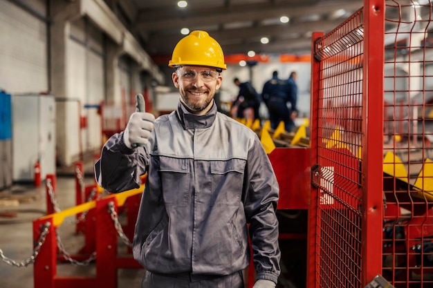 Un lavoratore dell'industria pesante sta alzando il pollice mentre sorride alla telecamera nella struttura