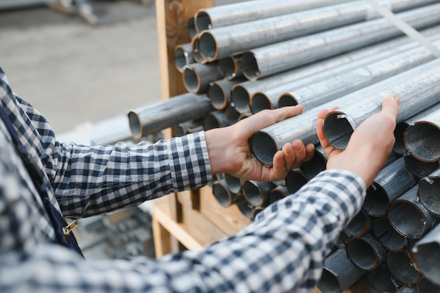 Un lavoratore detiene tubi metallici in un magazzino di fabbrica Laminazione di metalli