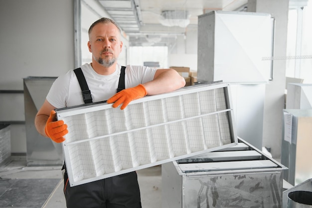 Un lavoratore di sesso maschile tiene un filtro dell'aria per l'aria condizionata in uno spazio ufficio Installazione di un condizionatore d'aria