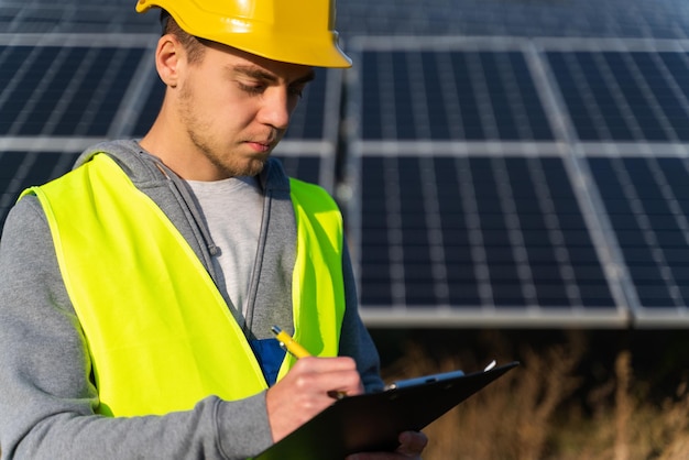 Un lavoratore di successo che indossa abiti protettivi che tiene una lavagna per appunti che prende appunti energia di fonte di pannelli solari Concetto di energia verde