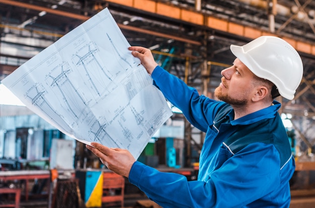 Un lavoratore in tuta e un elmetto bianco esamina il disegno