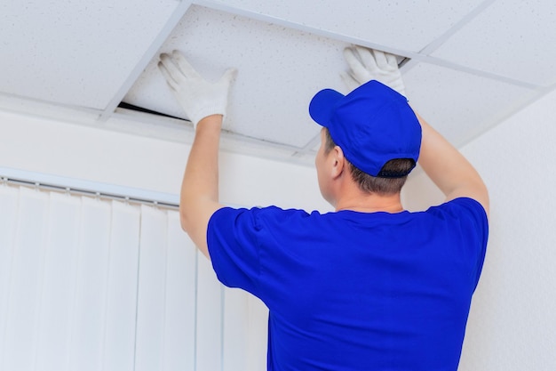 Un lavoratore in tuta installa un pannello del controsoffitto in cartongesso in uno spazio ufficio