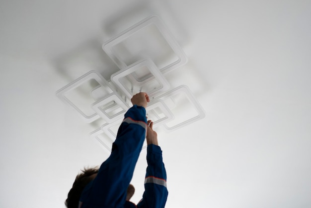 Un lavoratore in uniforme blu che ripara la luce a led a casa