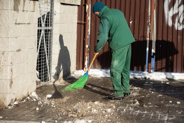 Un lavoratore manuale spazza via i resti di neve da un marciapiede bagnato con una scopa