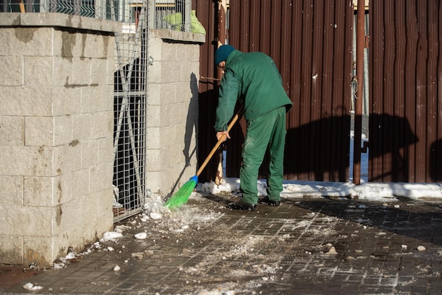 Un lavoratore manuale spazza via i resti di neve da un marciapiede bagnato con una scopa