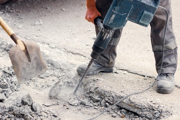 Un lavoratore ripara il manto stradale con un martello pneumatico in una giornata estiva Lavori di costruzione sulla strada