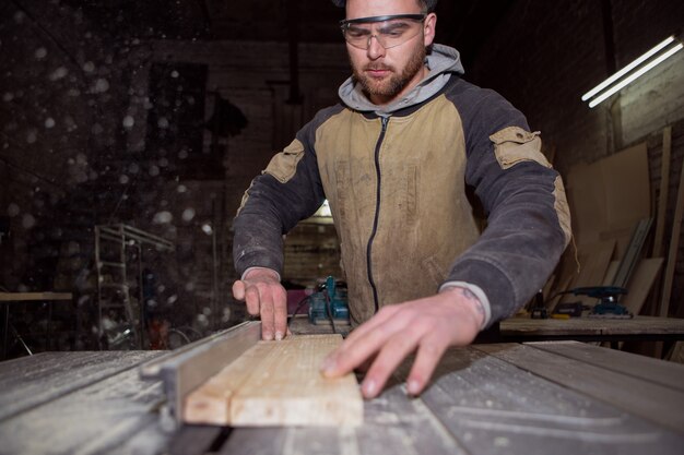 Un lavoratore si sta concentrando sulla lavorazione di una tavola di legno su una macchina circolare