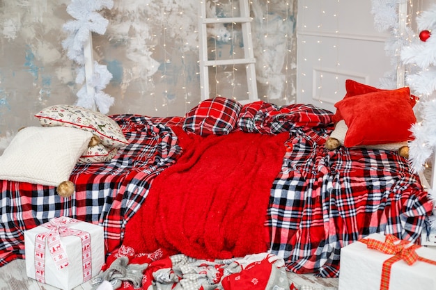 Un letto con decorazioni di Capodanno, copriletti rossi e ghirlande gialle. Decorare la casa per Natale