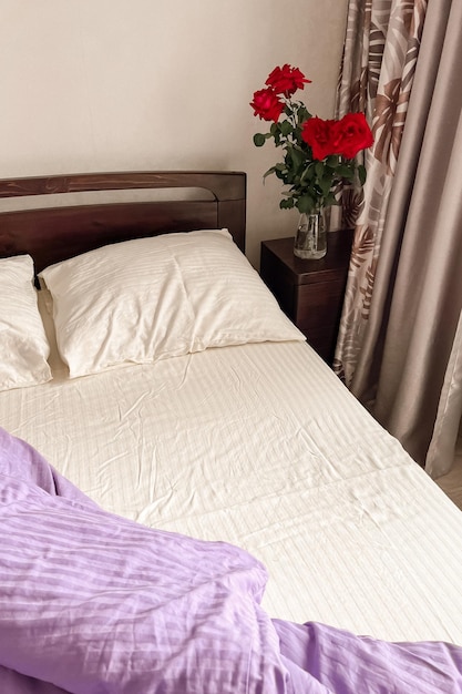 Un letto scuro con lenzuola bianche e lilla si trova accanto a un comodino su cui c'è un vaso di vetro con un mazzo di rose Il concetto di buongiorno Vista dall'alto