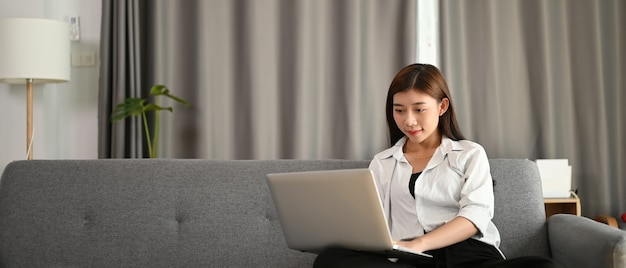 Un libero professionista in abiti casual sta lavorando al laptop e seduto sul divano nel soggiorno