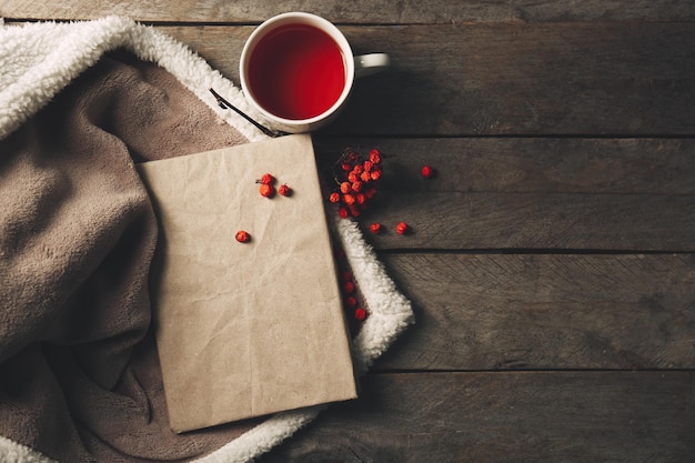 Un libro una tazza di bacche di sorbo del tè e una coperta sullo sfondo di legno