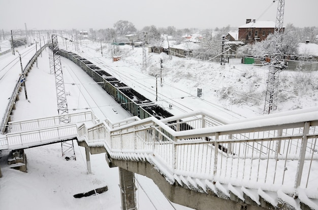 Un lungo treno di vagoni merci si muove lungo il binario della ferrovia. Paesaggio ferroviario in inverno dopo nevicate