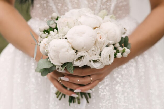 Un lussuoso bouquet da sposa con peonie bianche nelle mani della sposa